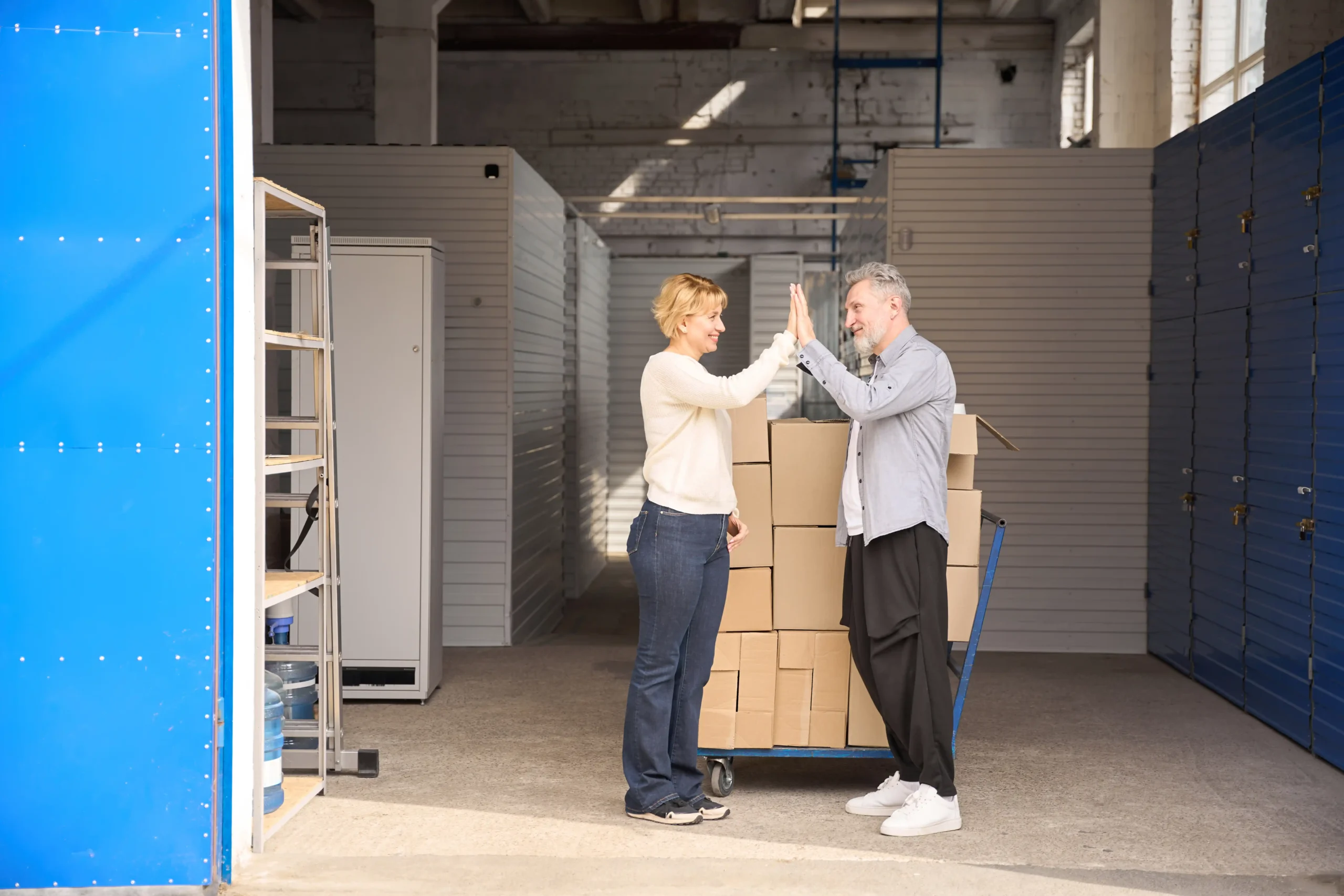A couple celebrating successful organization in a small storage facility with boxed inventory, showing how little warehouse storage improves workflow.
