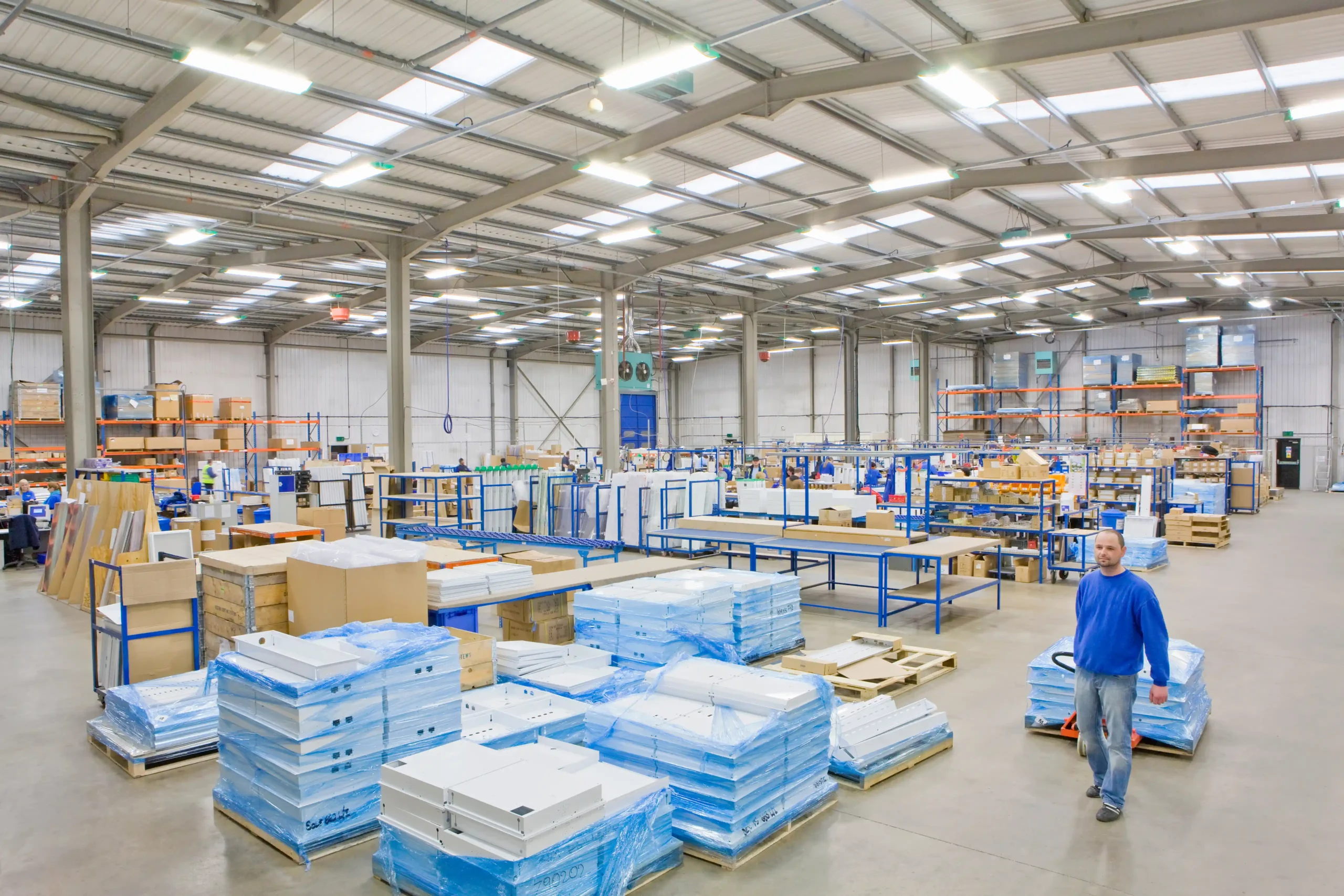 A worker moves palletized products inside a large warehouse storage facility with organized racks and open floor space.