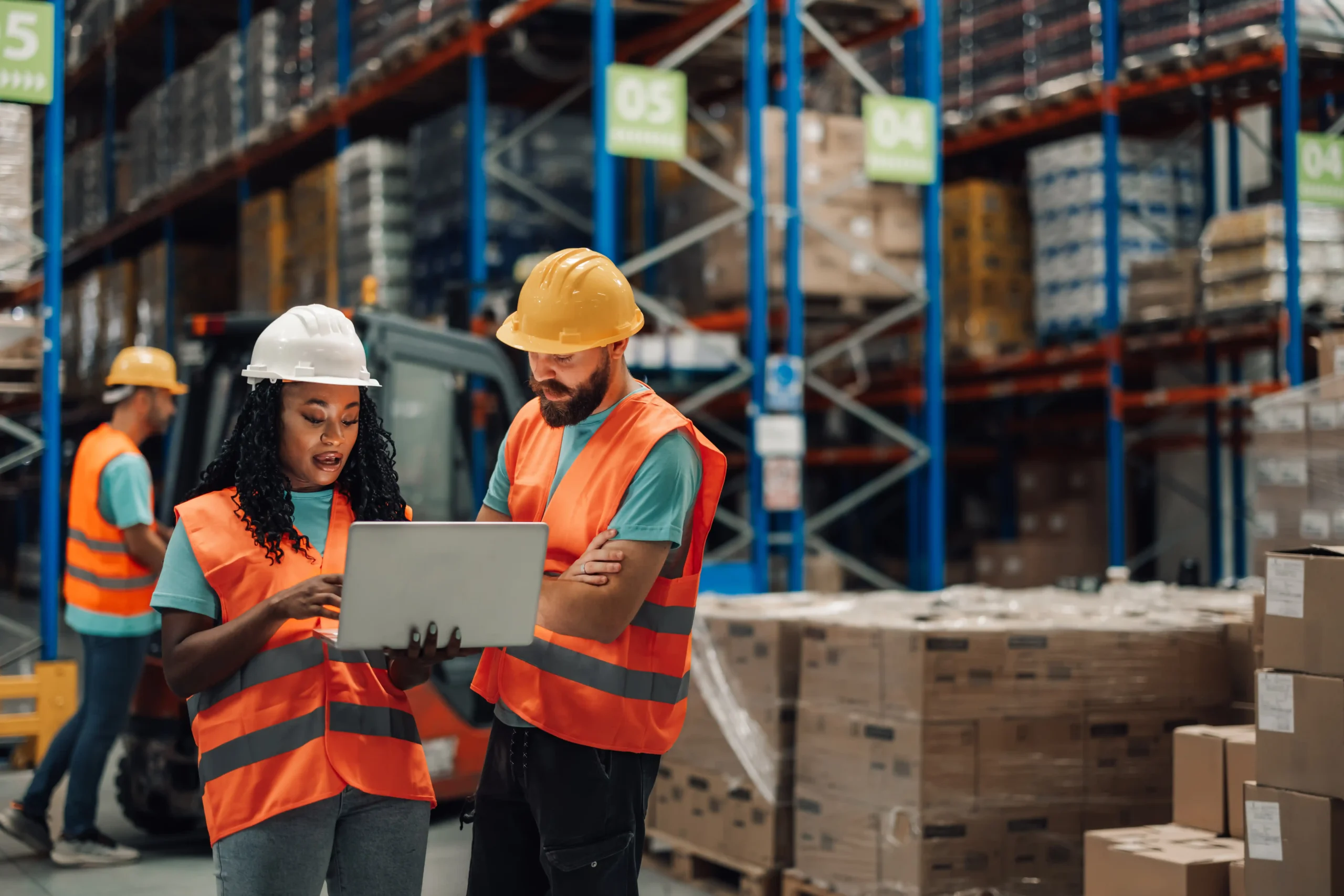 Warehouse team using a laptop on the floor to track inventory locations and orders with warehouse storage management software.