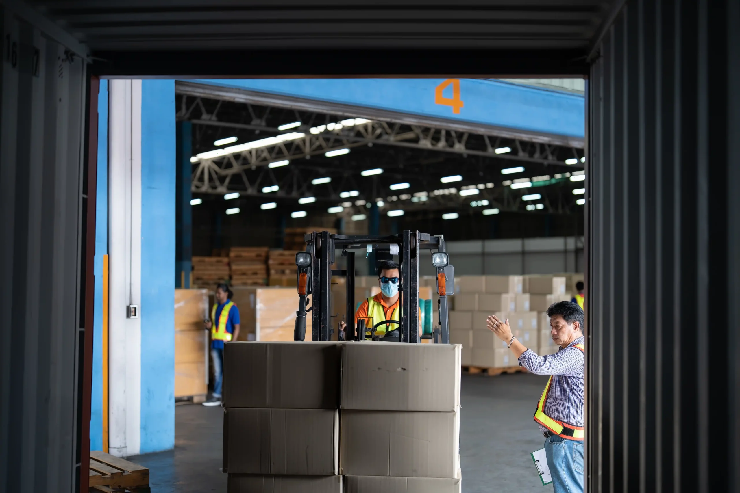Worker guiding a forklift as it loads boxes inside a facility offering small warehouse storage for rent.