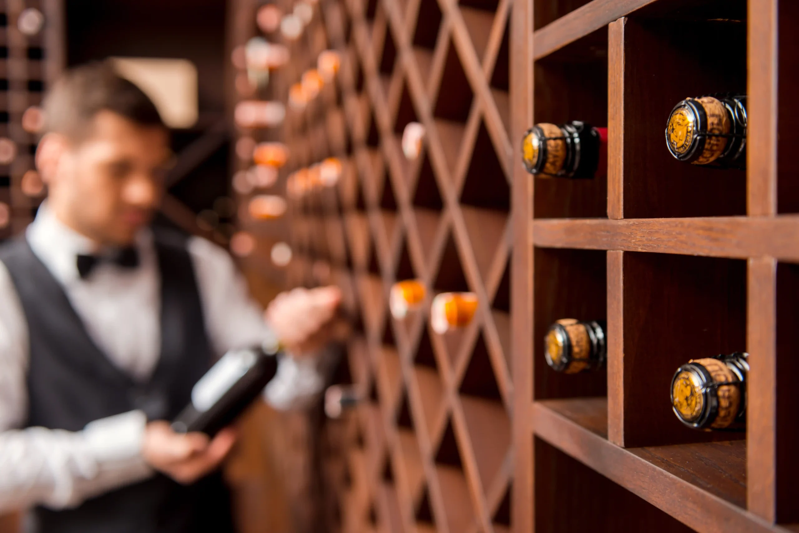A sommelier selecting a bottle from a wooden rack system inside a commercial wine storage room designed for safe inventory management.