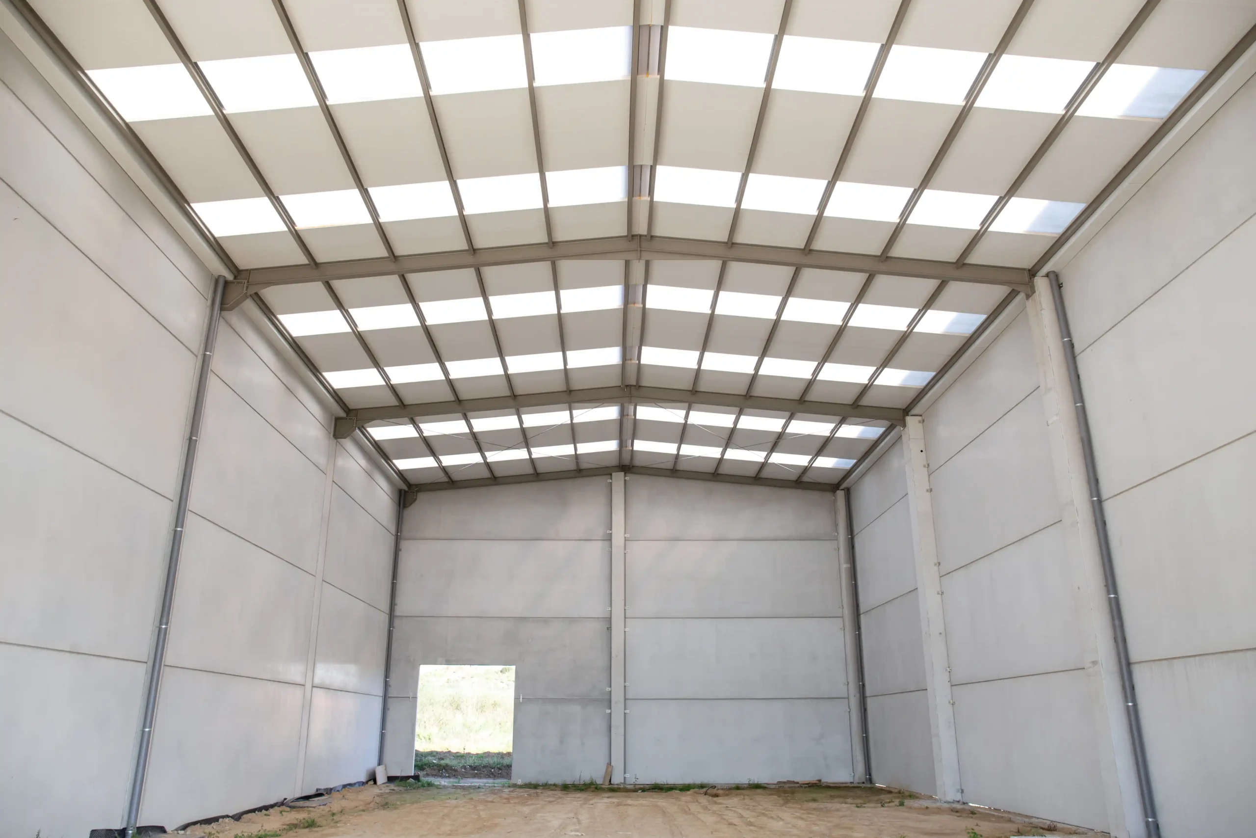 Empty warehouse storage tent with high steel frame walls and translucent roof panels for durable weather-protected storage.