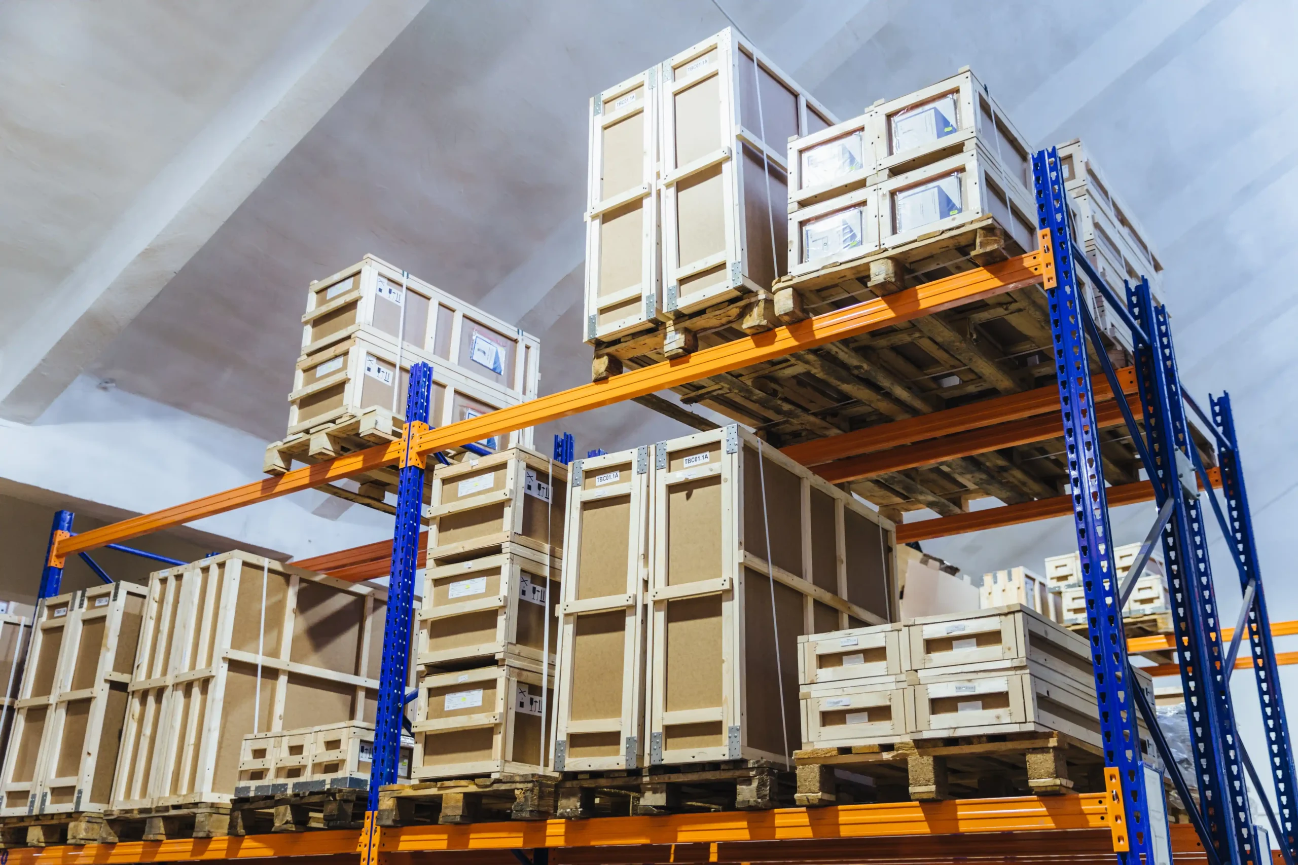 Large warehouse storing wooden crates and palletized goods in secure areas supported by warehouse storage cages.