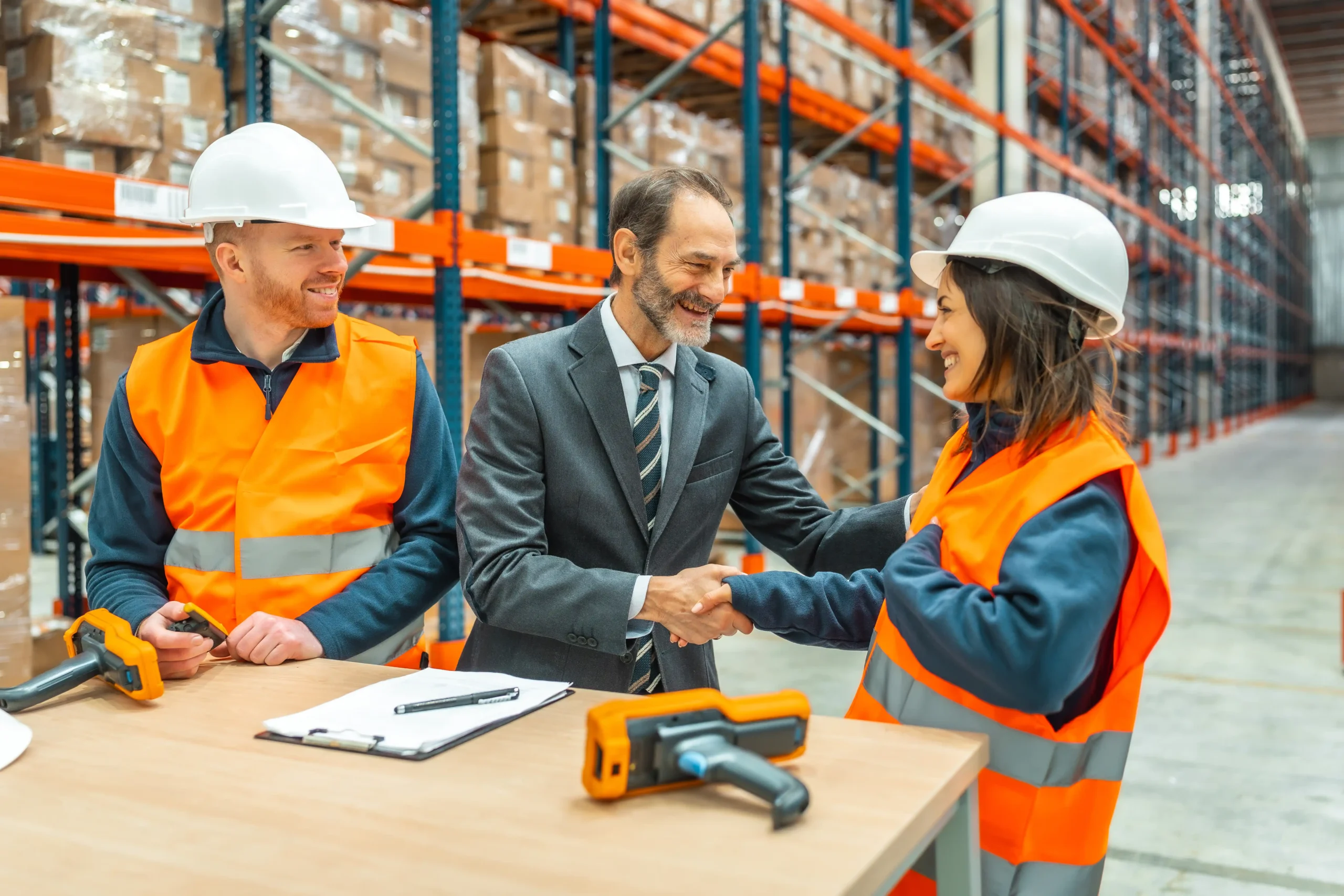 Warehouse manager shaking hands with workers in safety gear as they finalize details of a warehouse storage agreement inside a distribution center.