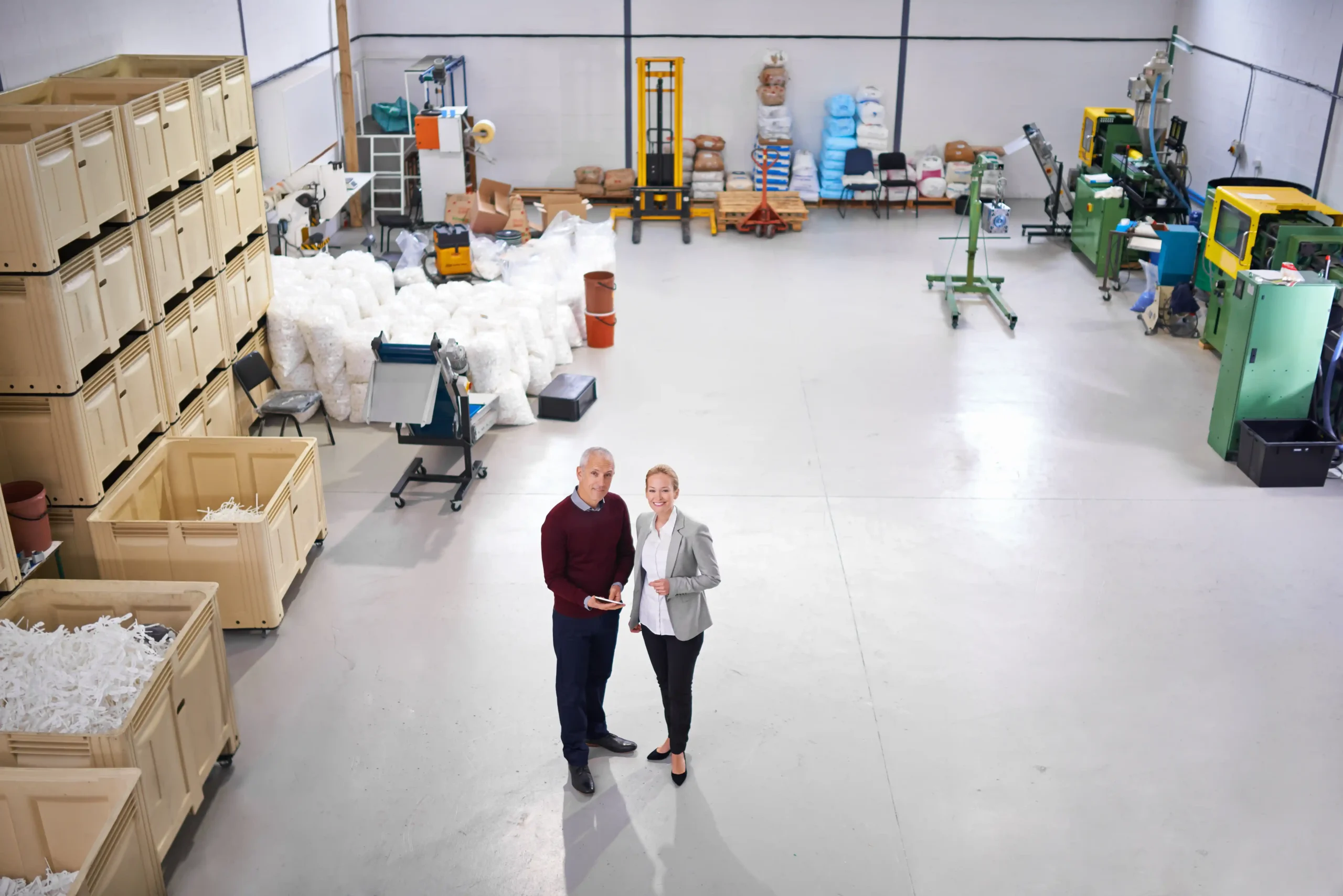 Supervisors reviewing warehouse storage layout inside a spacious facility with large stackable bins and equipment