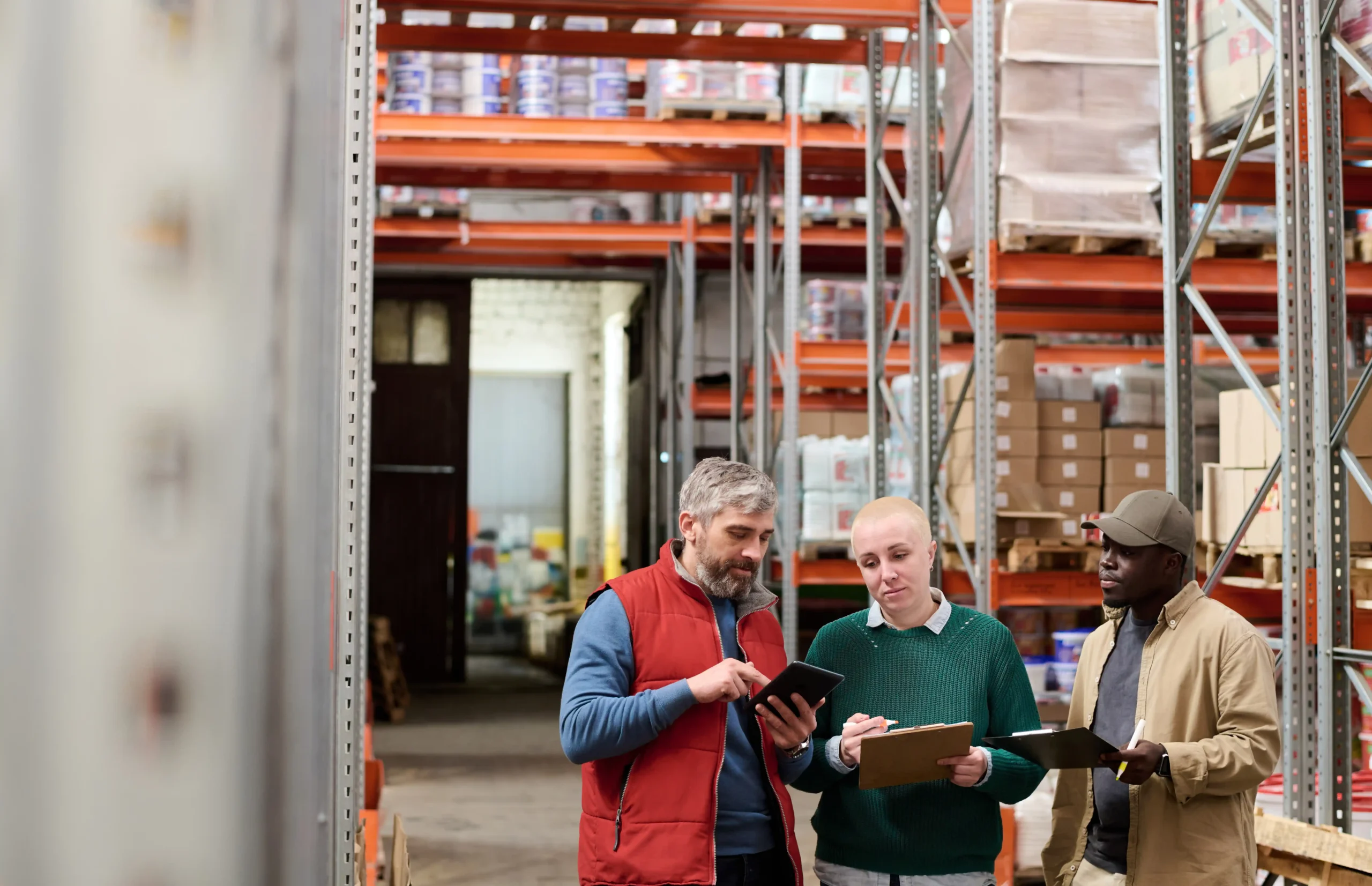 A group of warehouse employees reviewing digital inventory data in the aisles, demonstrating how an automated warehouse storage system enhances tracking and decision-making.