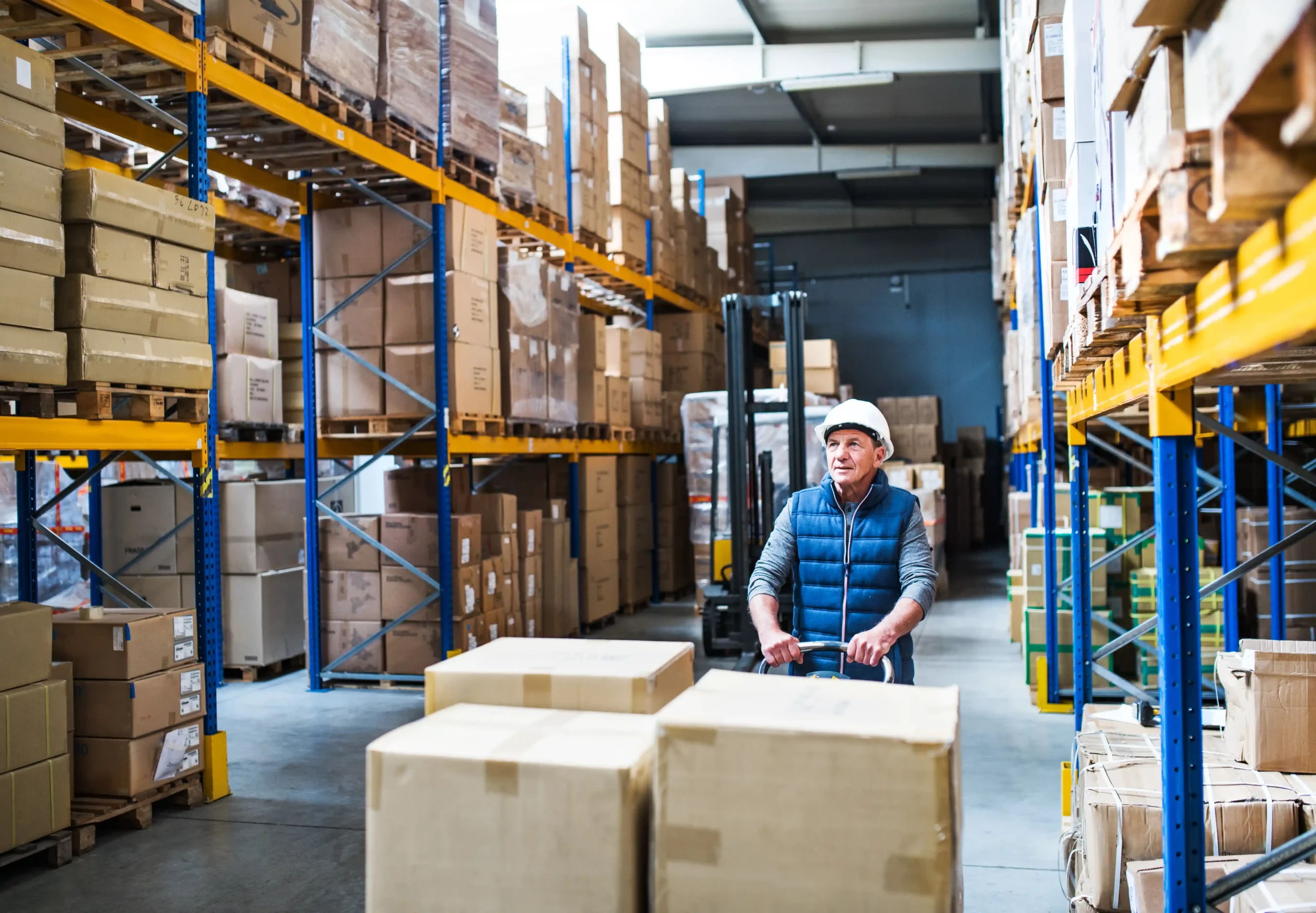 Senior warehouse worker transporting boxes through organized aisles in a small warehouse storage for rent location.