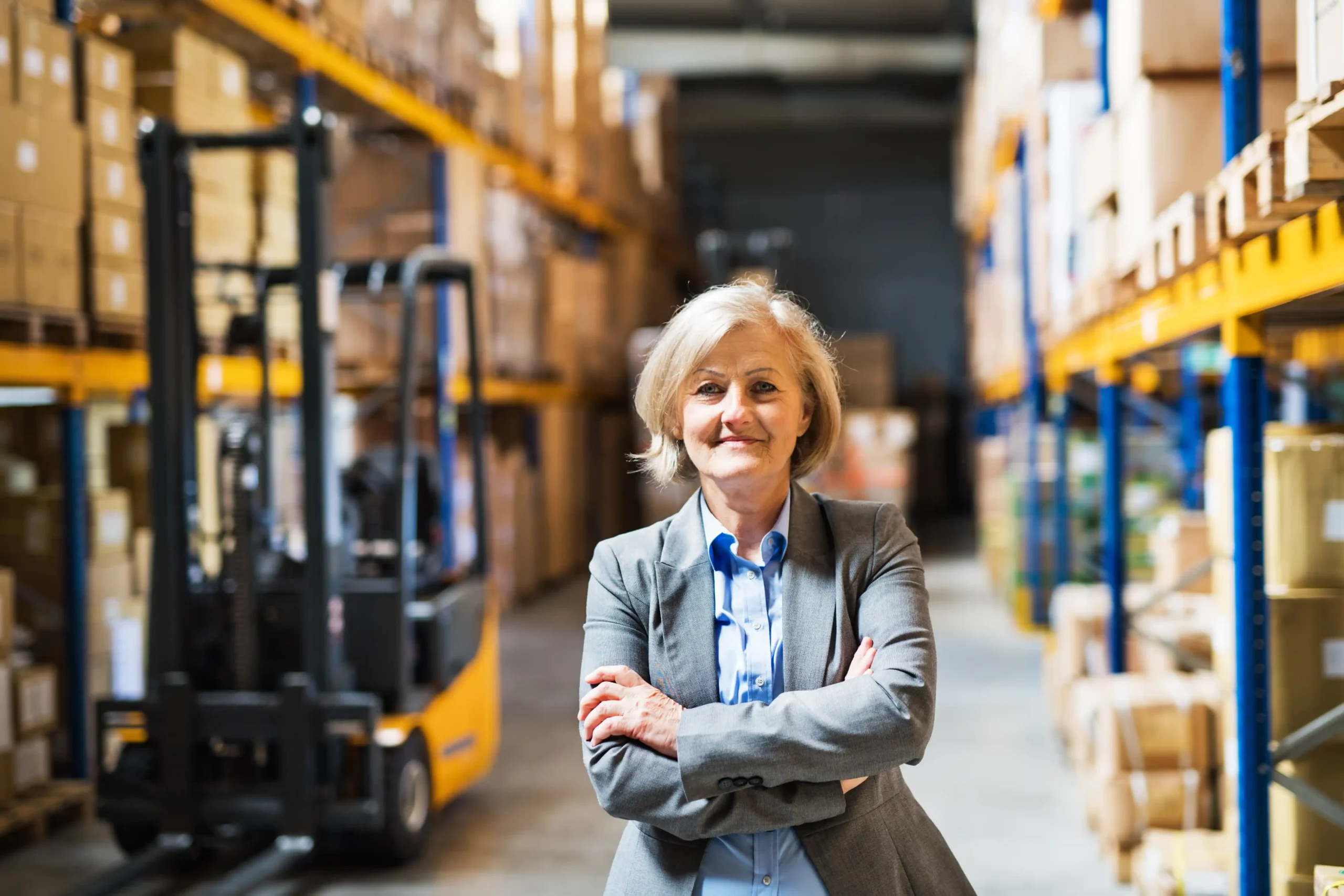 Warehouse and logistics specialist supervising warehouse operations with forklifts and palletized inventory in the background