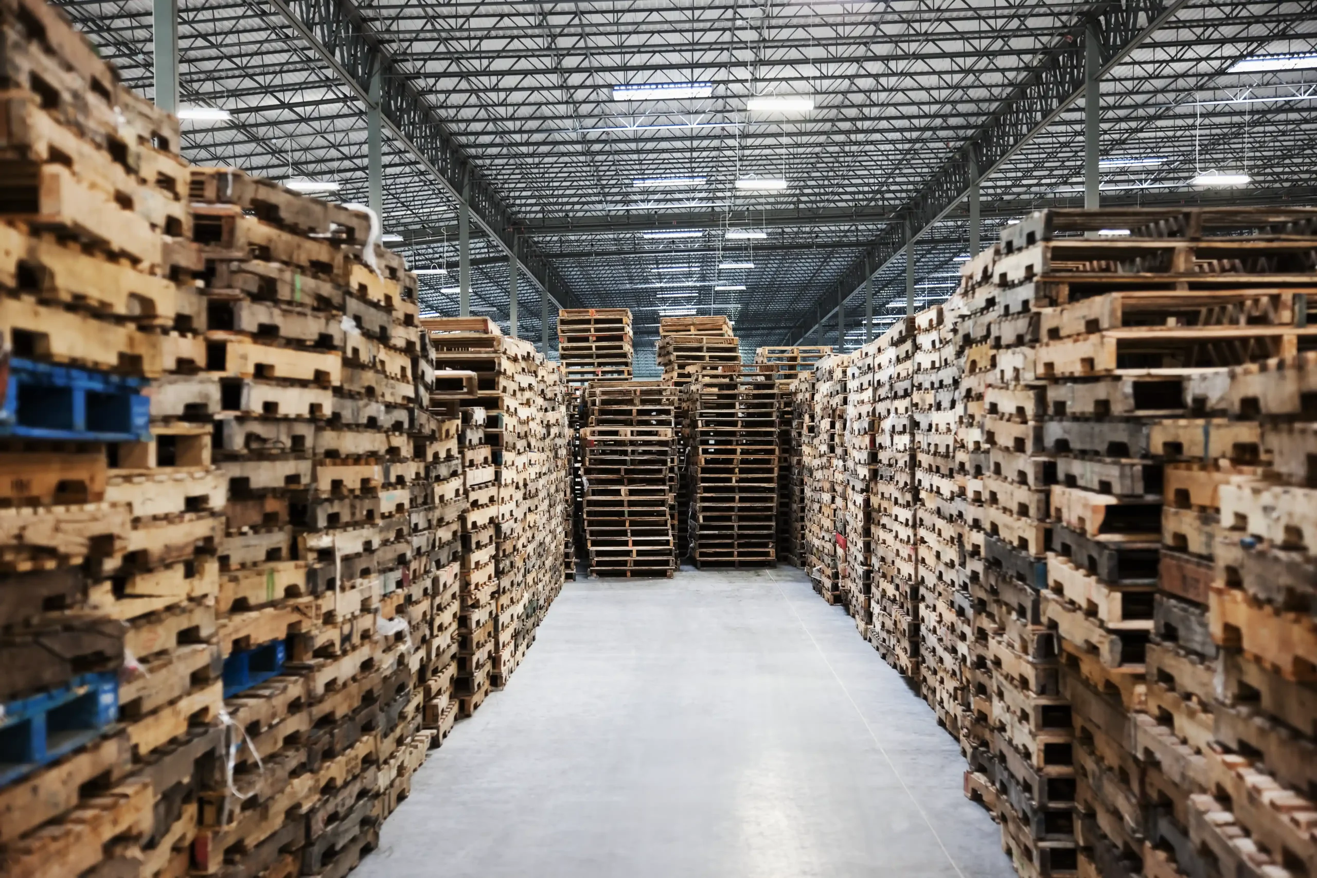 Rows of stacked wooden pallets inside a warehouse, demonstrating space utilization and how it affects warehouse storage rates per pallet.