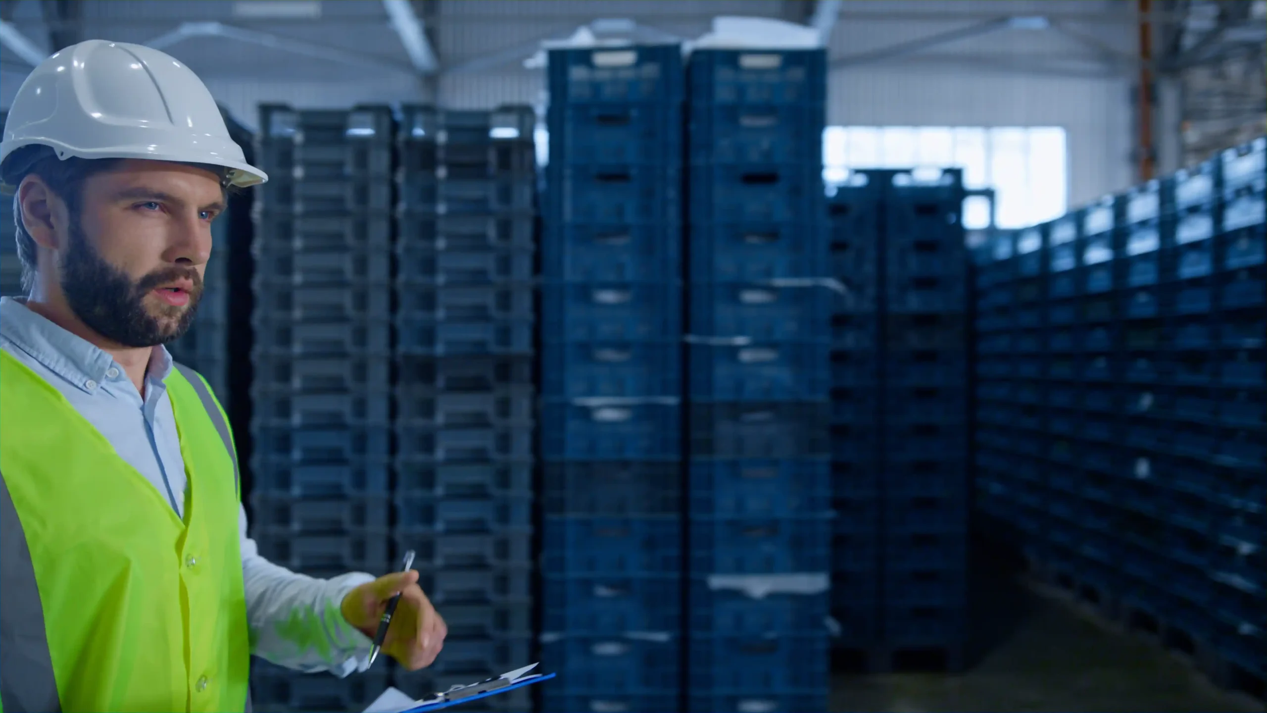 Warehouse manager assessing tall stacks of warehouse storage crates for inventory accuracy.
