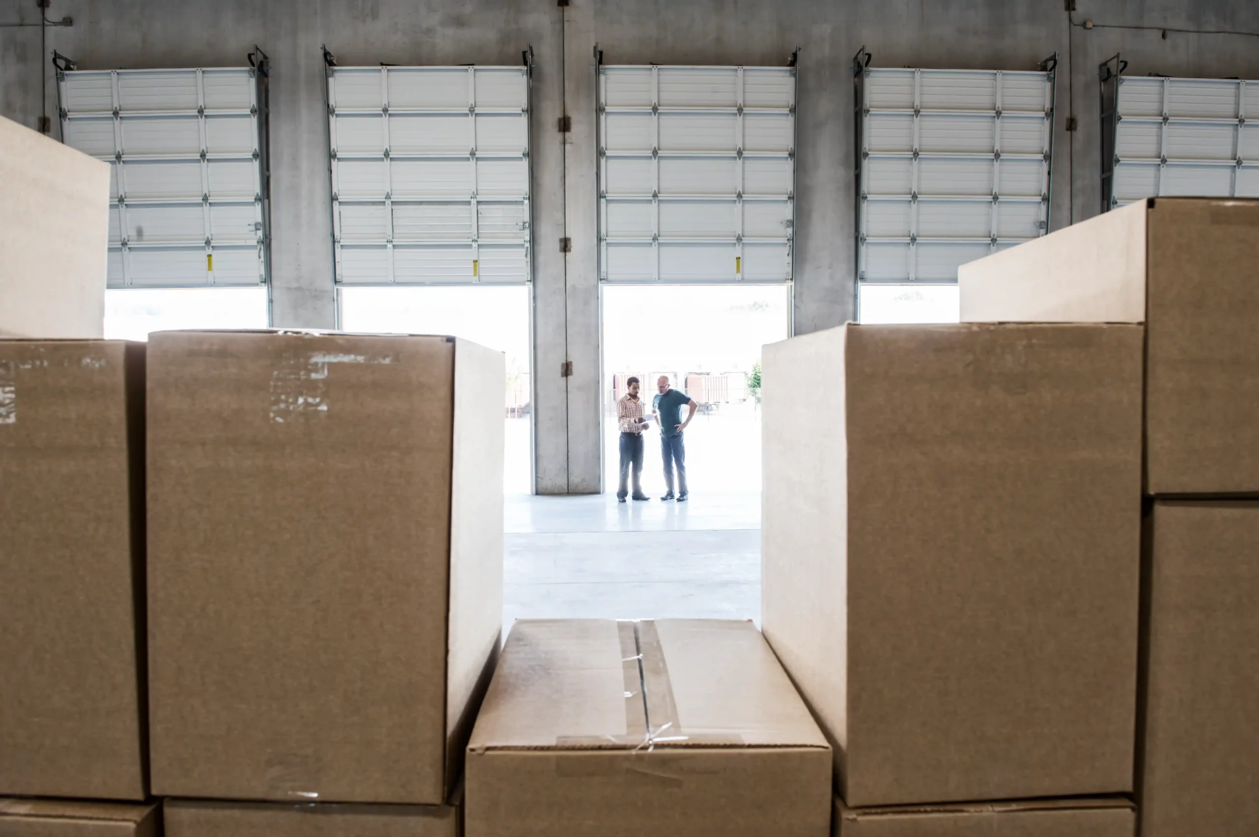 Workers inspecting and preparing boxed goods at a loading dock as part of long term warehouse storage procedures.