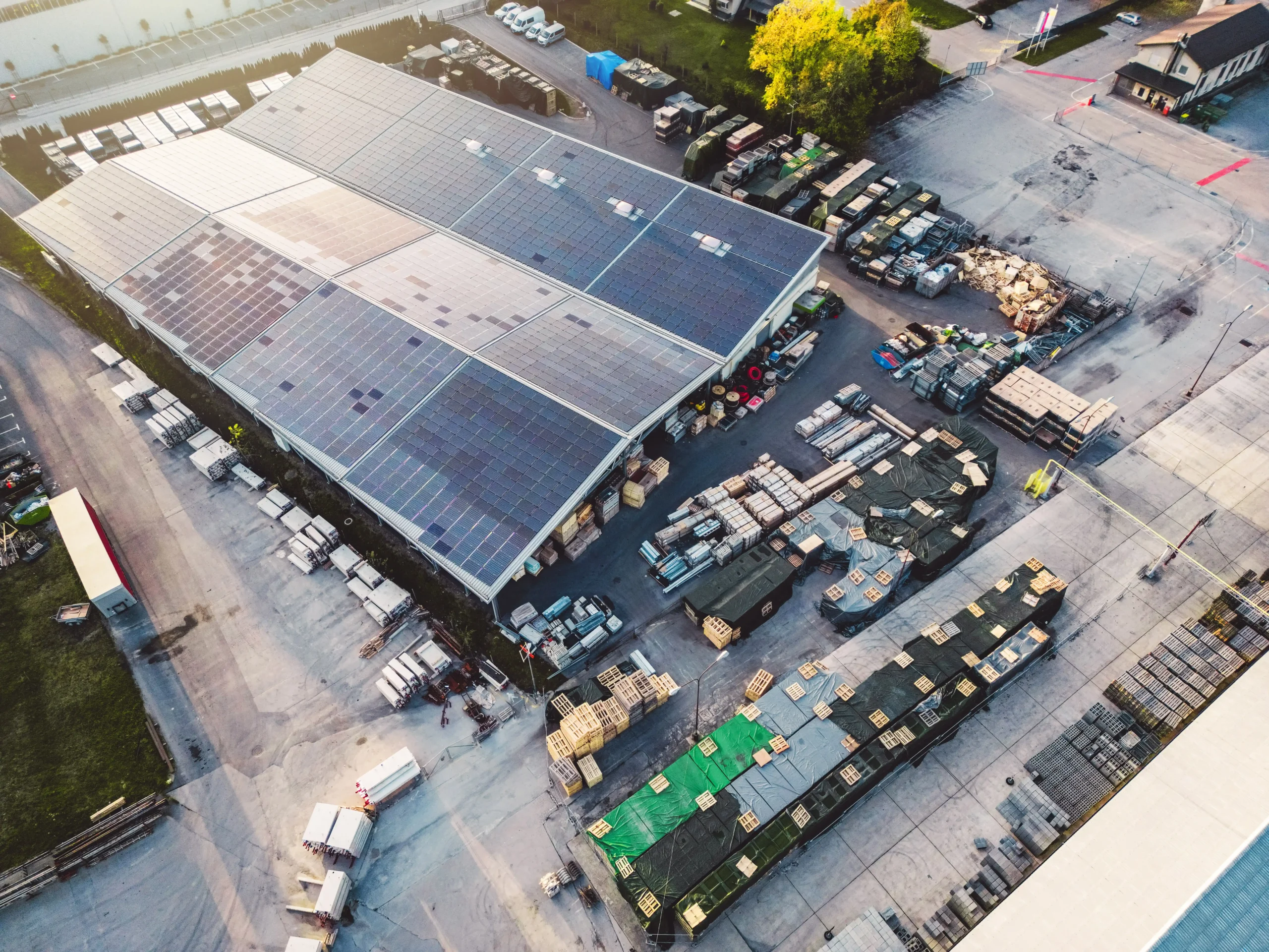 Drone view of a warehouse storage building covered in solar panels, surrounded by inventory and outdoor storage areas.