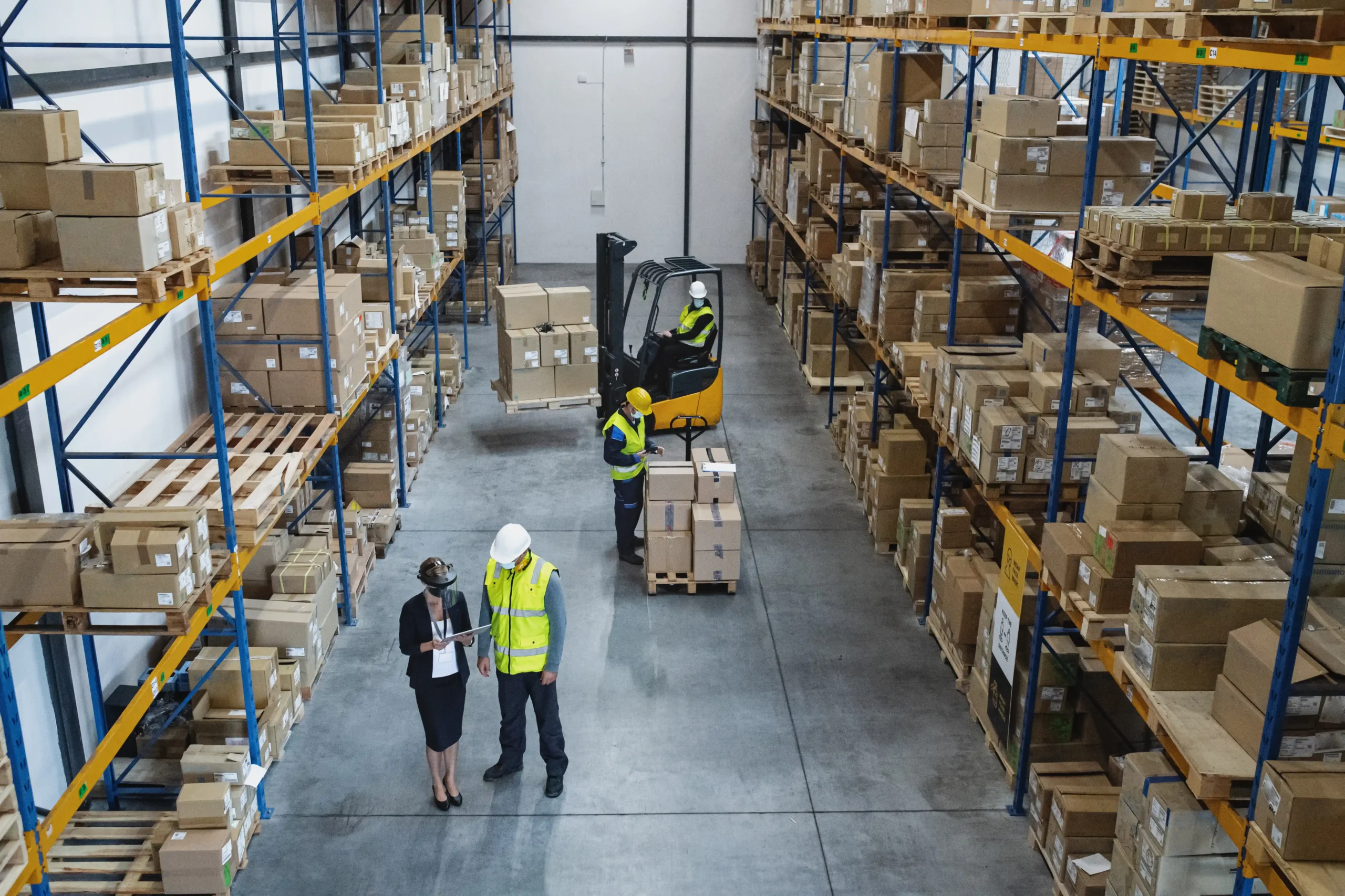 Overhead view of workers and forklifts operating among racking and shelving types of warehouse storage.