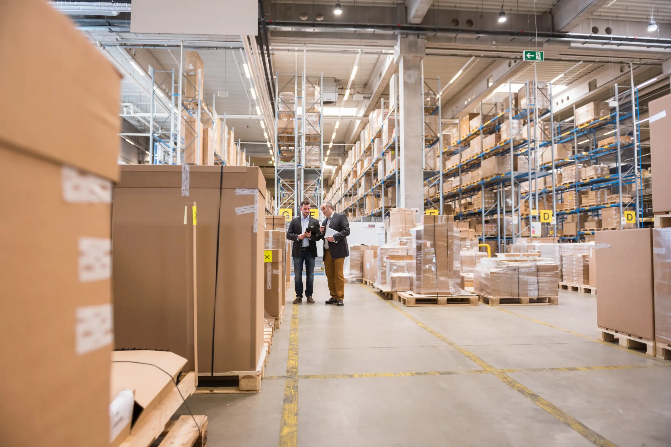 Two managers reviewing operations inside a large warehouse storage area lined with tall racks and packaged goods.