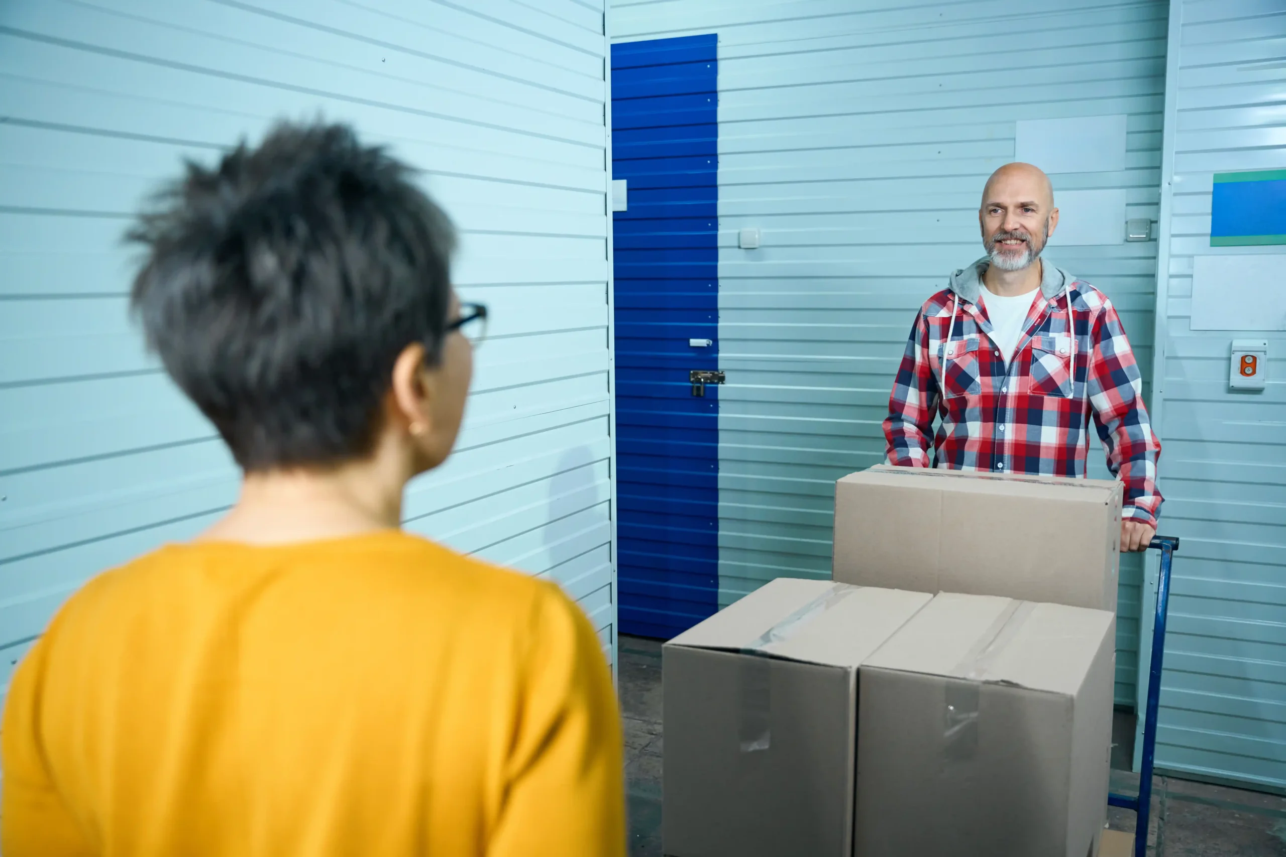 Two people moving boxes through a storage hallway within a secure small warehouse storage facility featuring modern unit design.