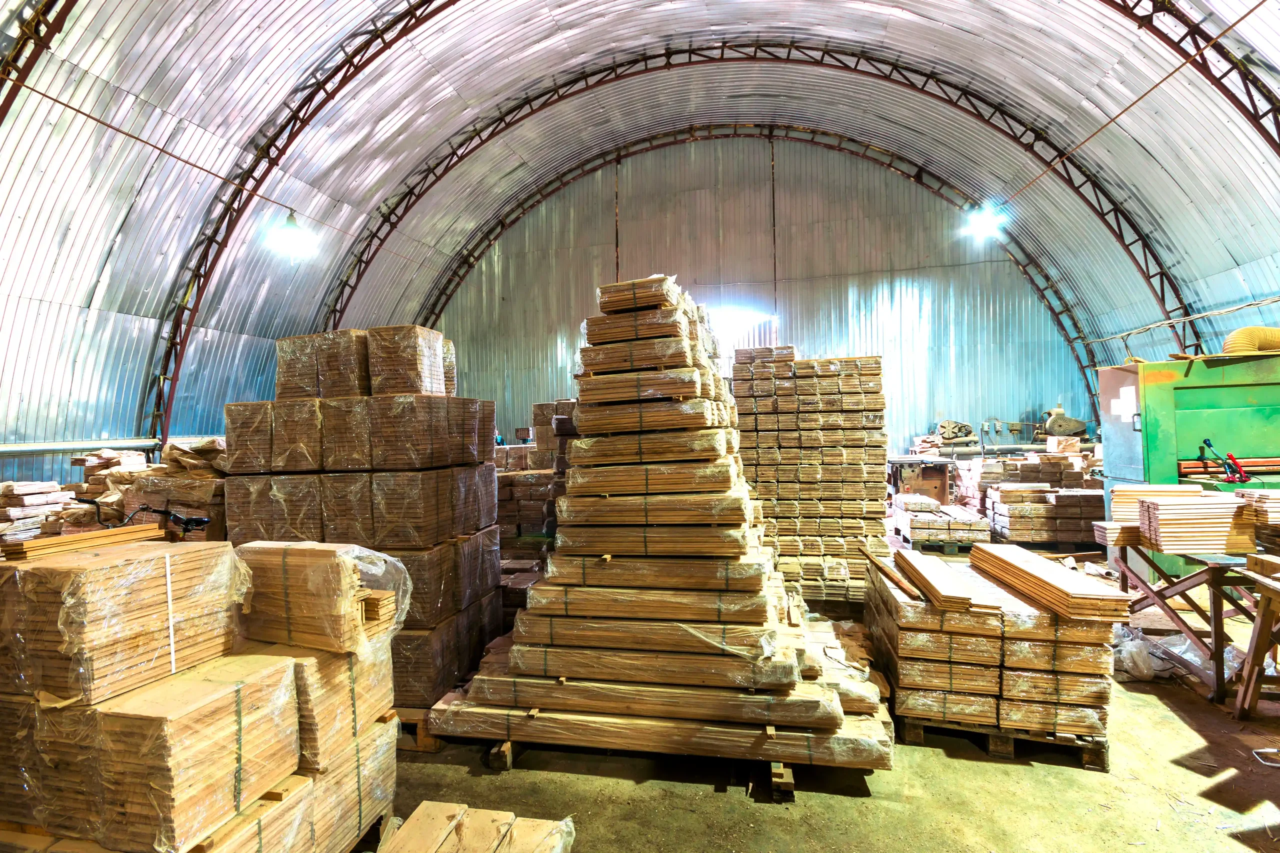 Arched warehouse storage tent filled with timber pallets and construction materials organized for industrial storage.