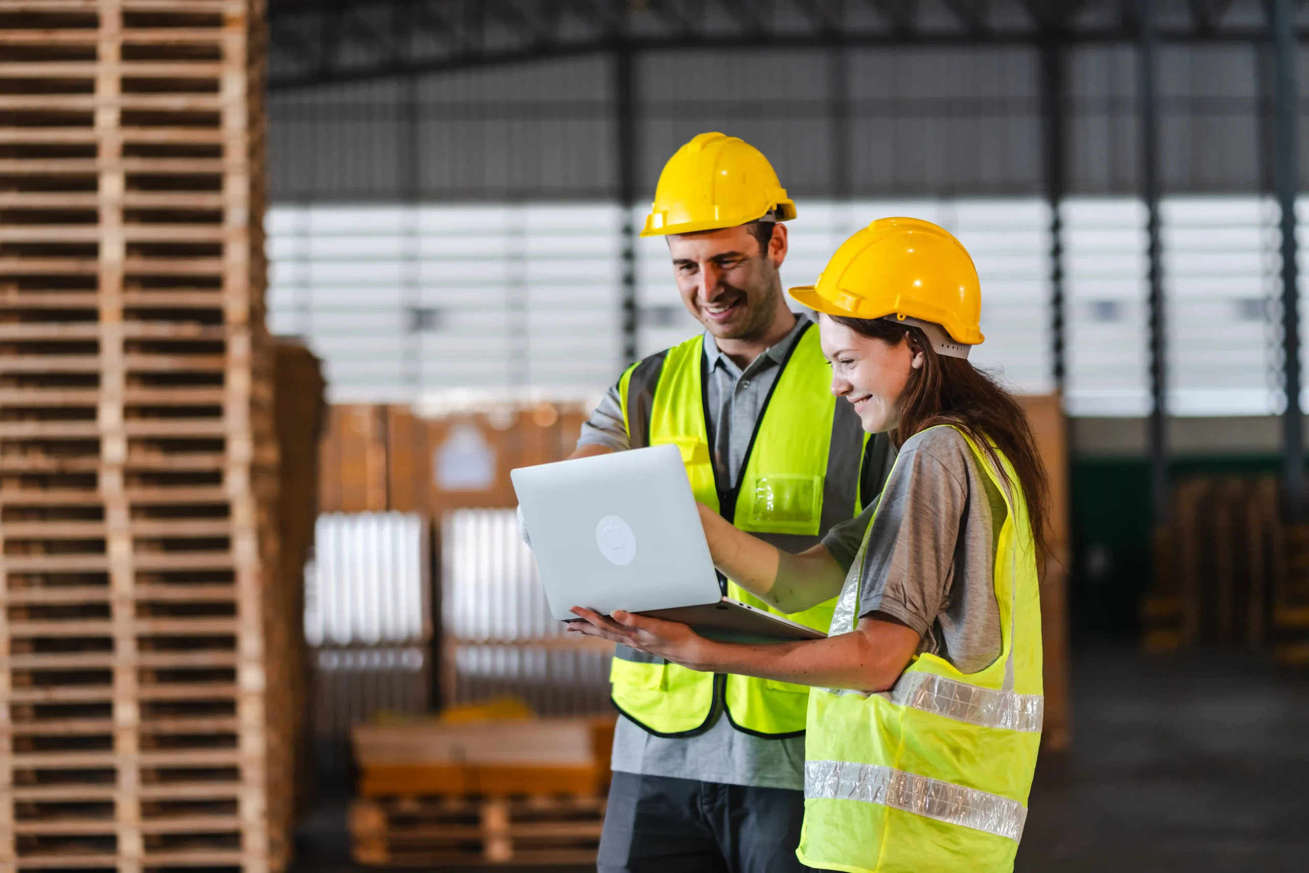 Warehouse logistics workers using a laptop to plan workflow in a facility filled with organized warehouse storage racking systems.