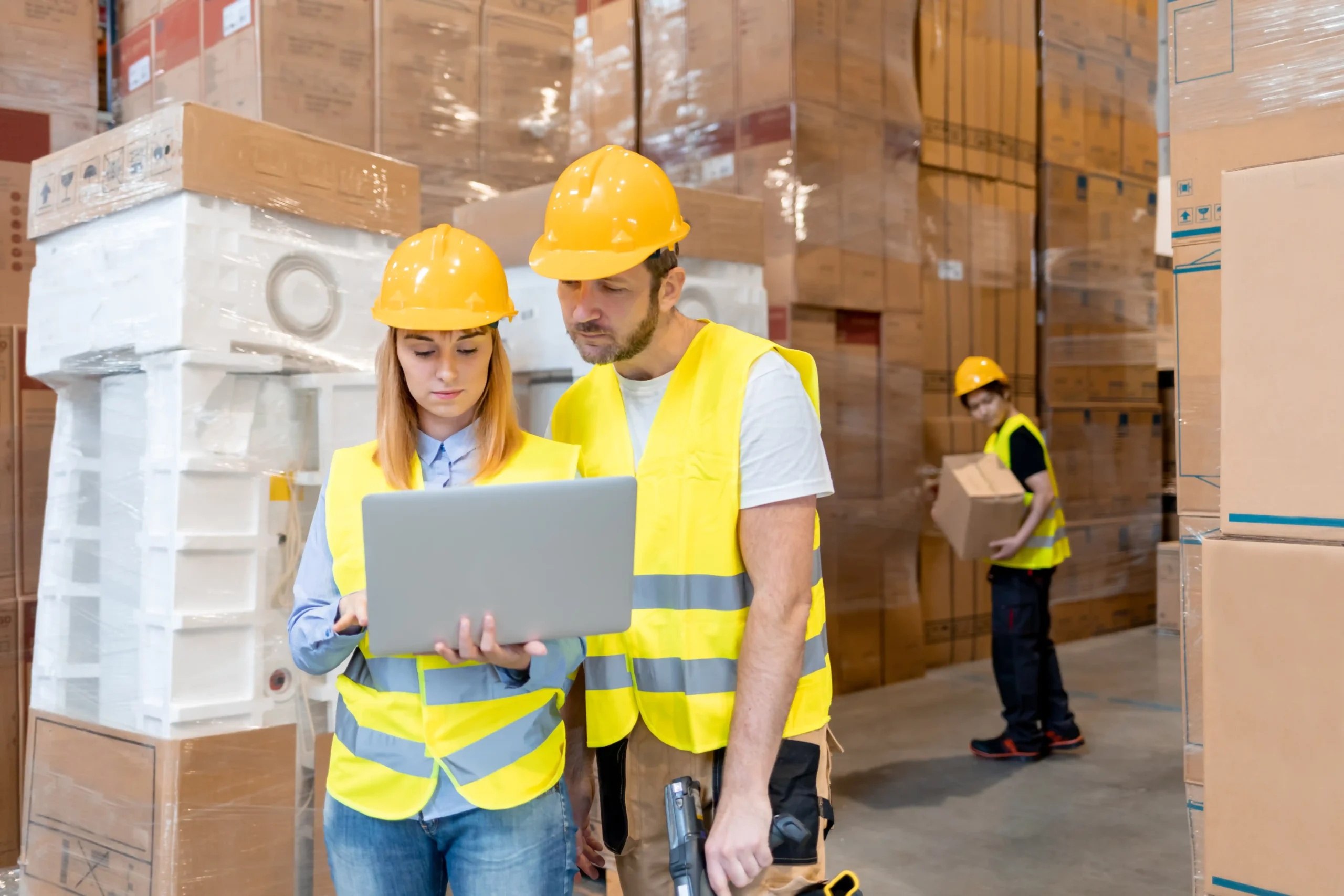 Two warehouse employees discussing delivery plans on a laptop while surrounded by tall warehouse storage racking systems.