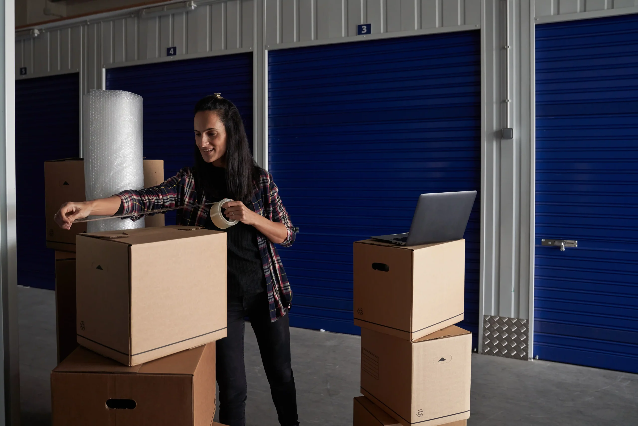 Woman packing cardboard boxes inside a self-storage unit, demonstrating how commercial storage insurance protects stored business property.